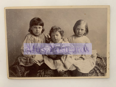 Vintage photograph of three children sitting together with a visible brand name.