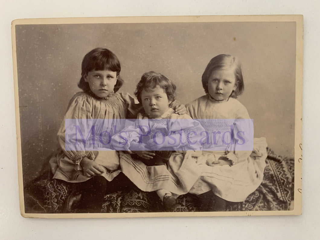 Vintage photograph of three children sitting together with a visible brand name.